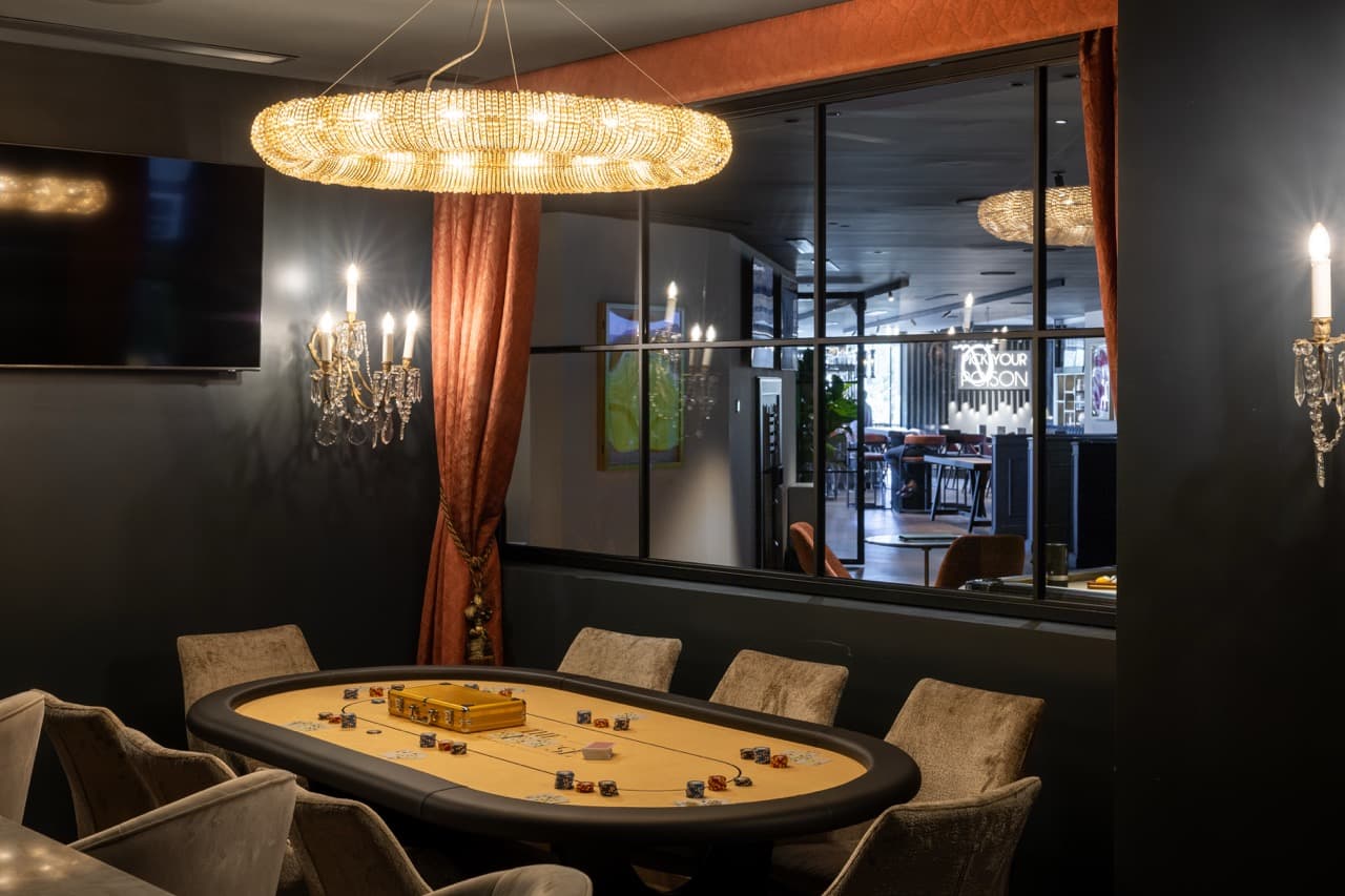 The Laurent-Perrier Players’ Lounge at the Clubhouse Marbella - illuminated champagne walls flank a wood-panelled hearth, Chesterfield armchairs facing in, low tungsten light.